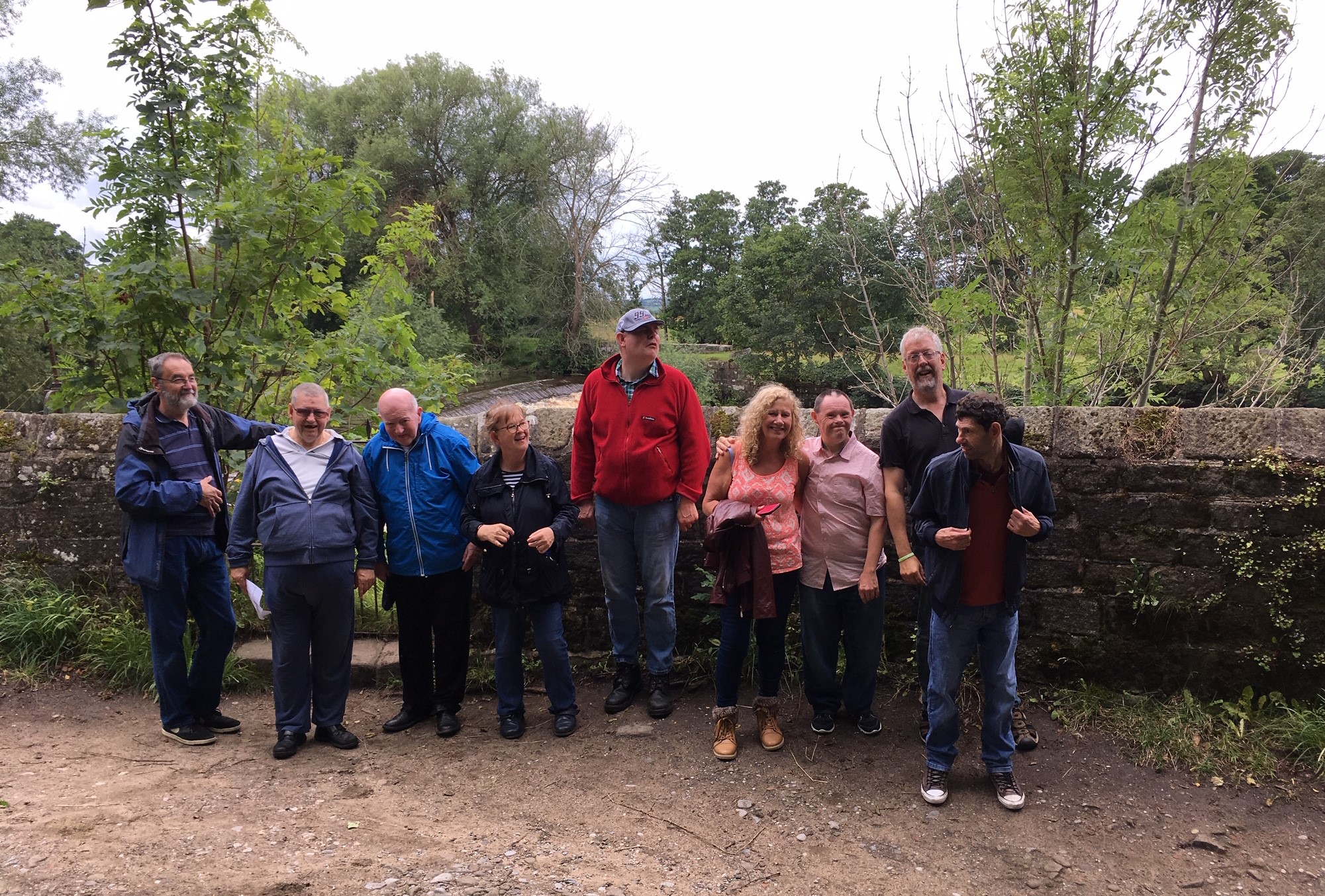 A group of people standing by a stone wall with trees behind.