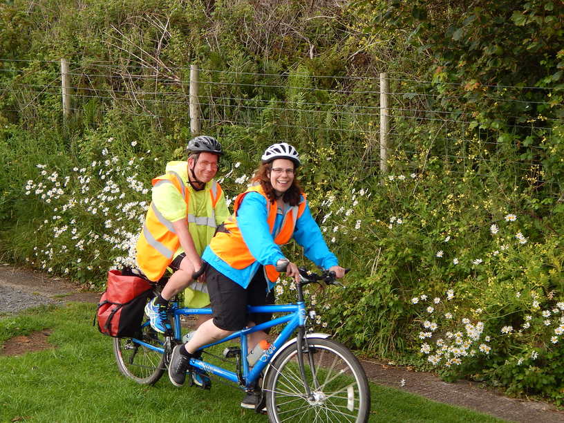 A woman piloting a tandem with a man on the back, riding down a country lane.