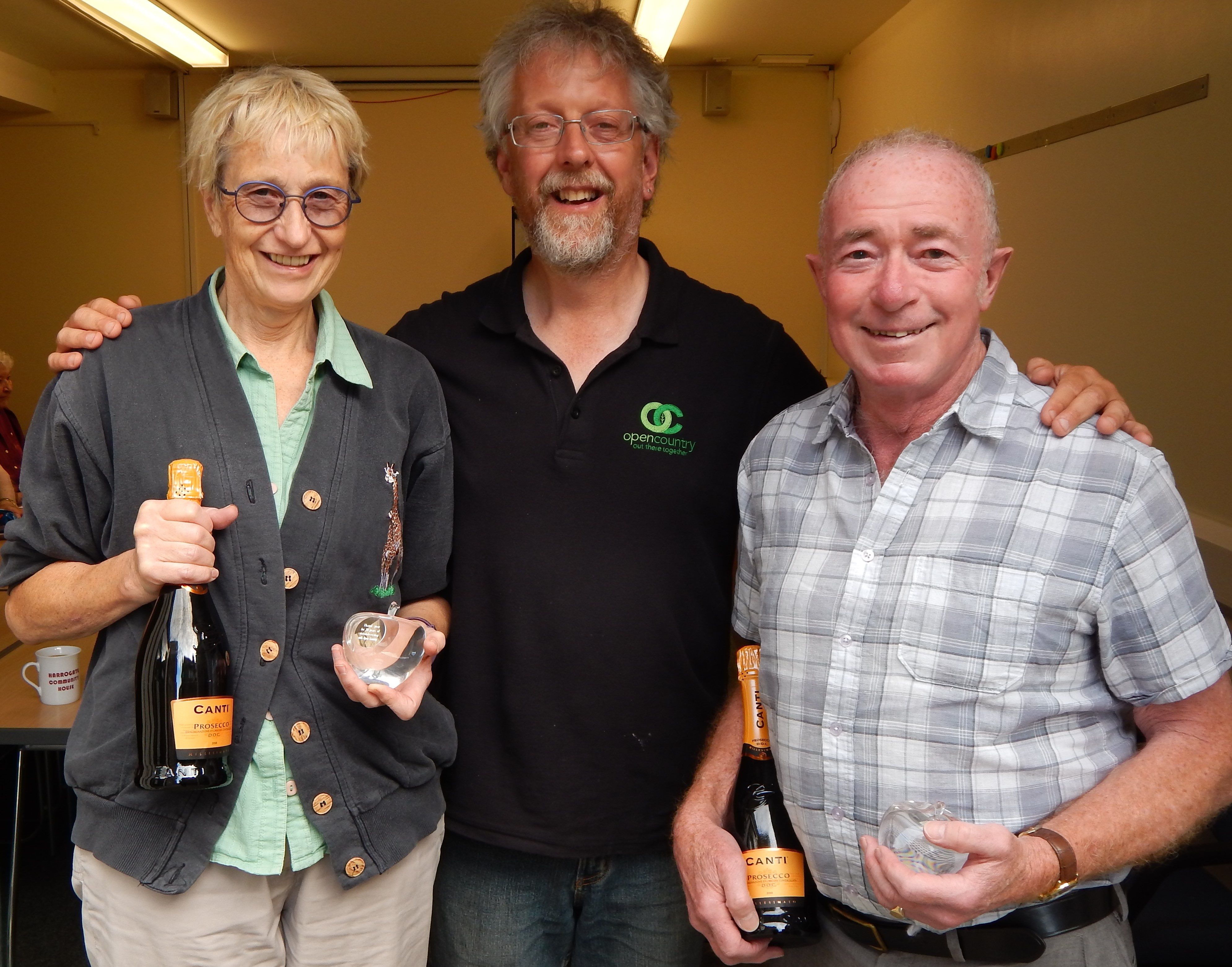 Two people holding bottles of champagne and glass apple awards.