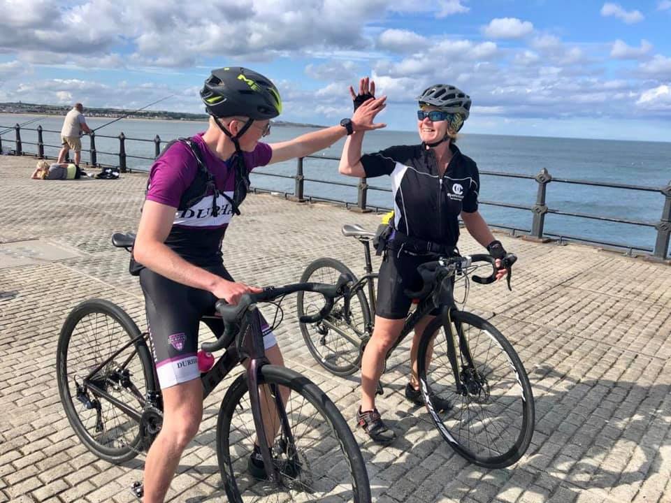 A man and woman on bikes by the sea high-fiving each other