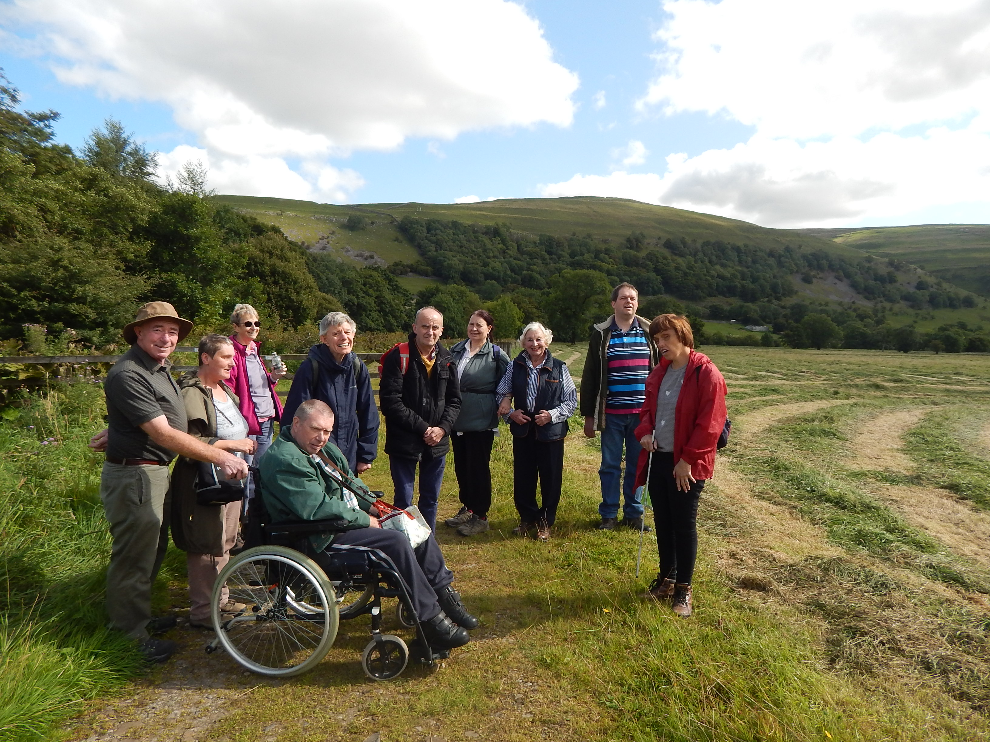 A group of people in a sunny field with trees and hills behind