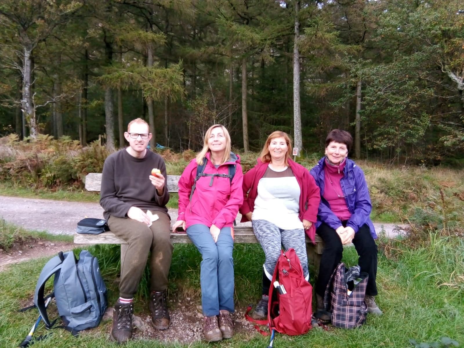 Four people sittong on a bench with woodland behind.