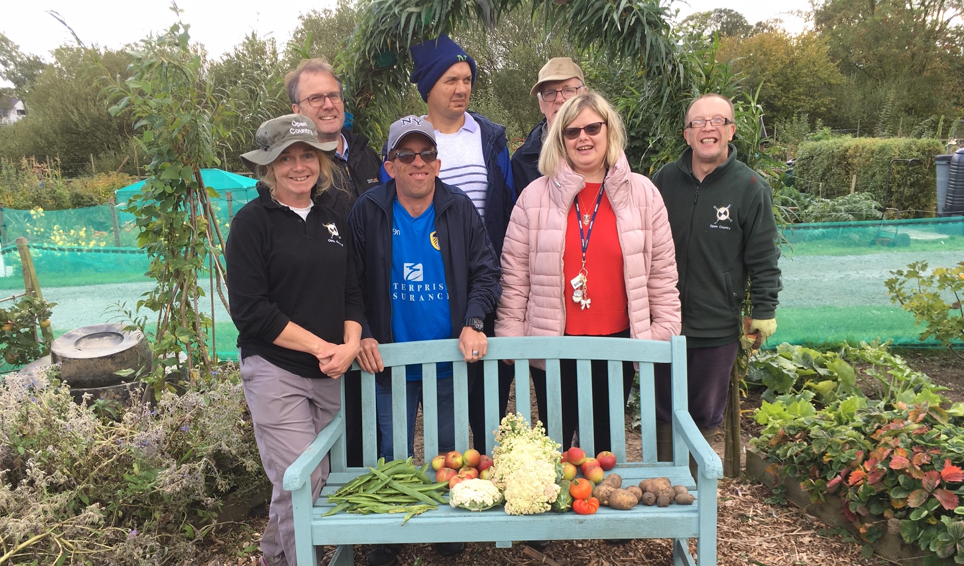 A group of people standing behind a bench with allotment produce on.