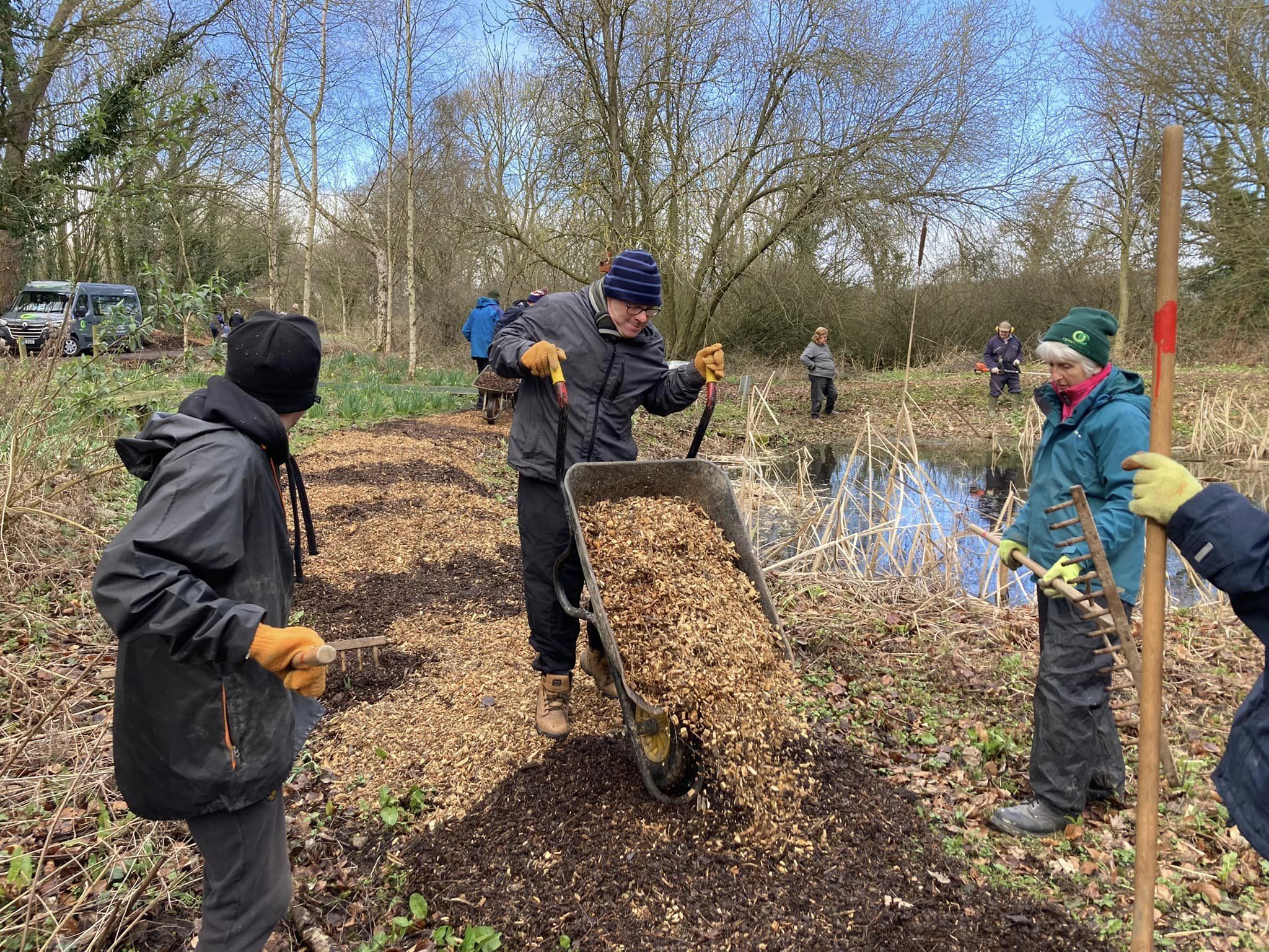 A group of people outdoors laying a woodchip path