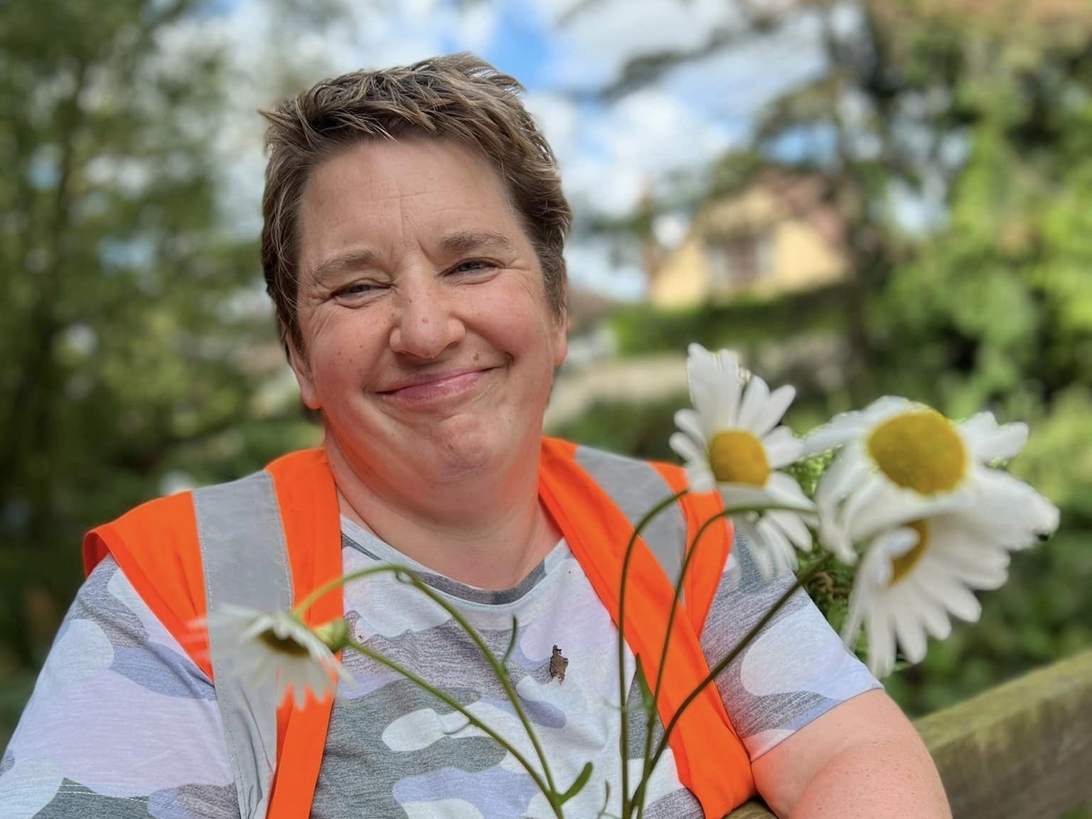 A woman smiling, holding some wild flowers