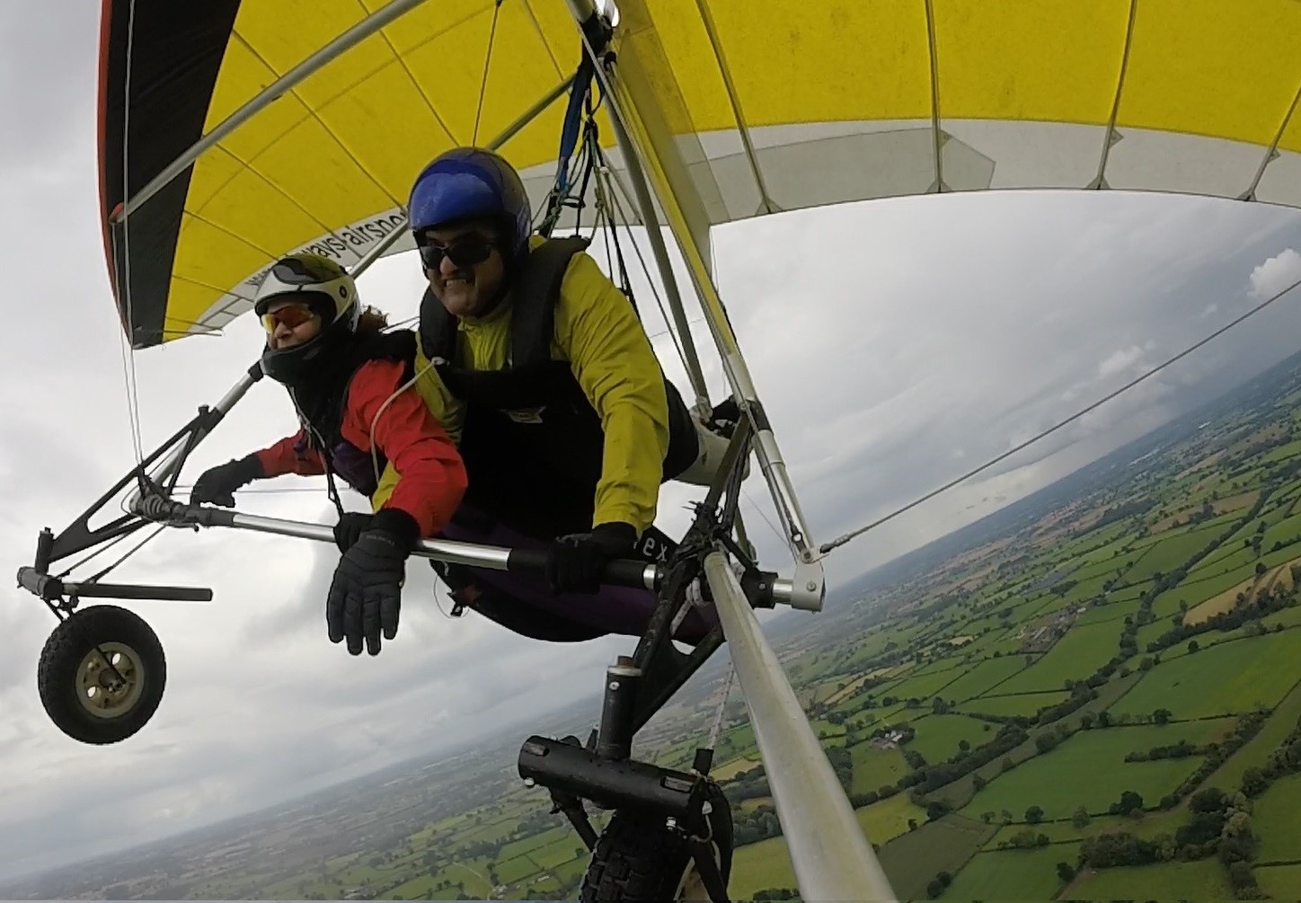 A man and a woman tandem hang gliding with hills below them