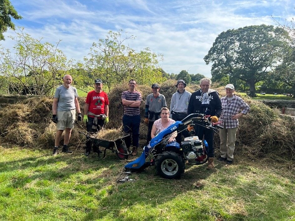 A group standing in a meadow in the summer with a mower