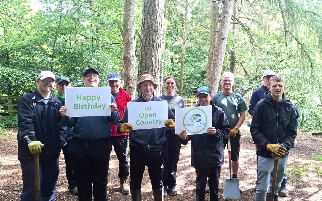 A group of people in a wood hold up signs wishing Open Country a happy birthday