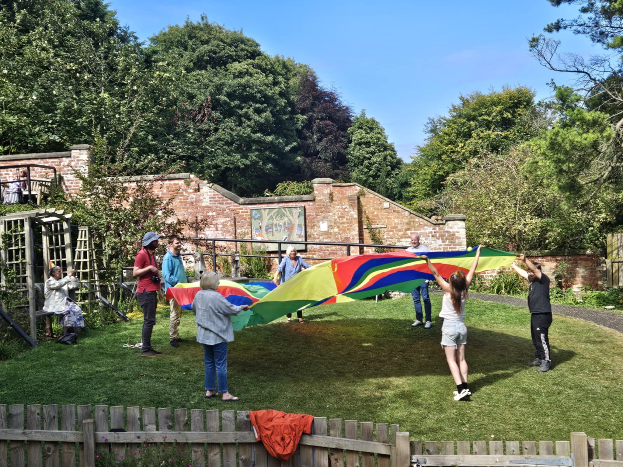 A group of people in a woodland garden playing with a colourful parachute