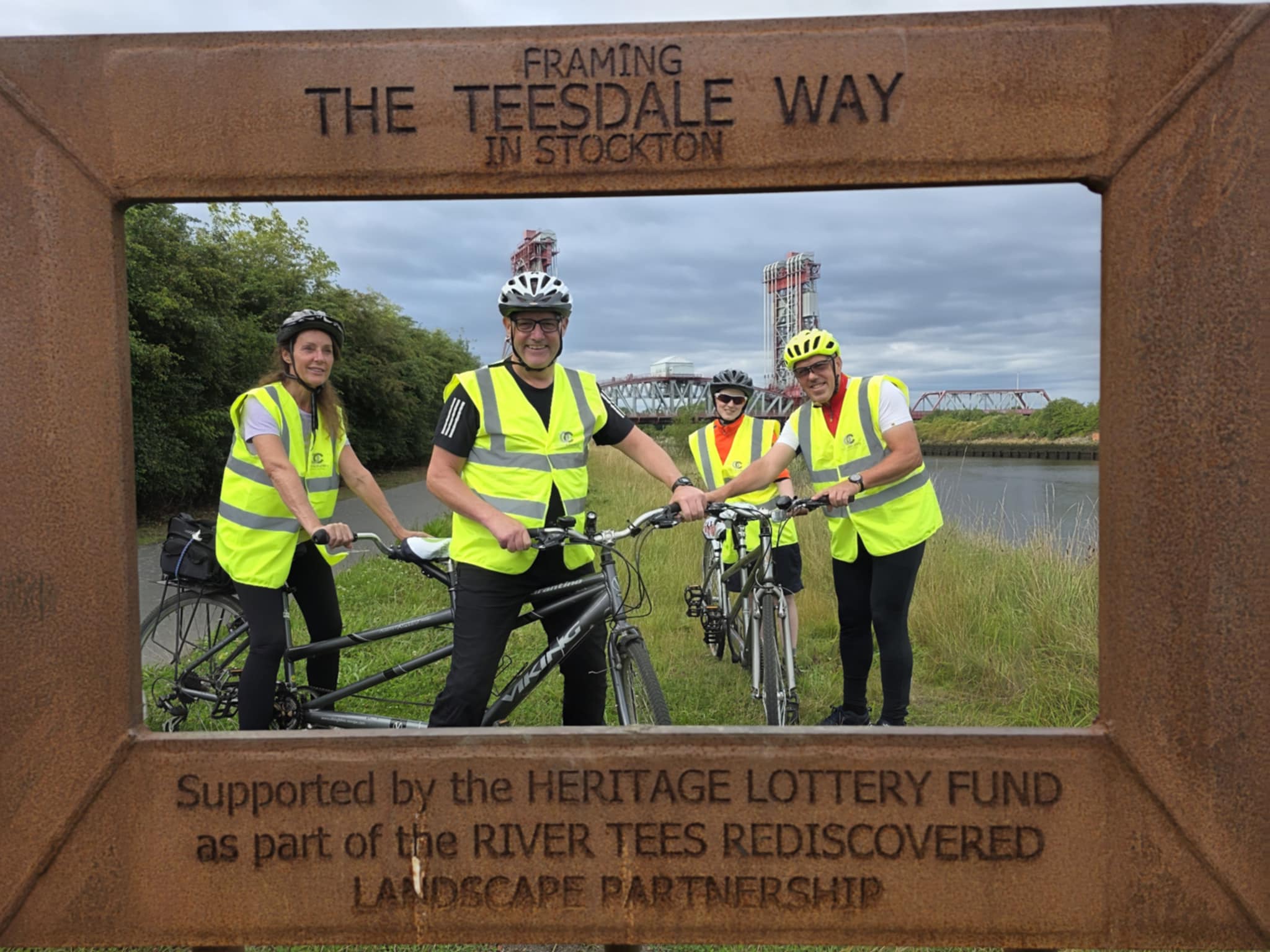 A group of tandem riders with a river and bridge behind