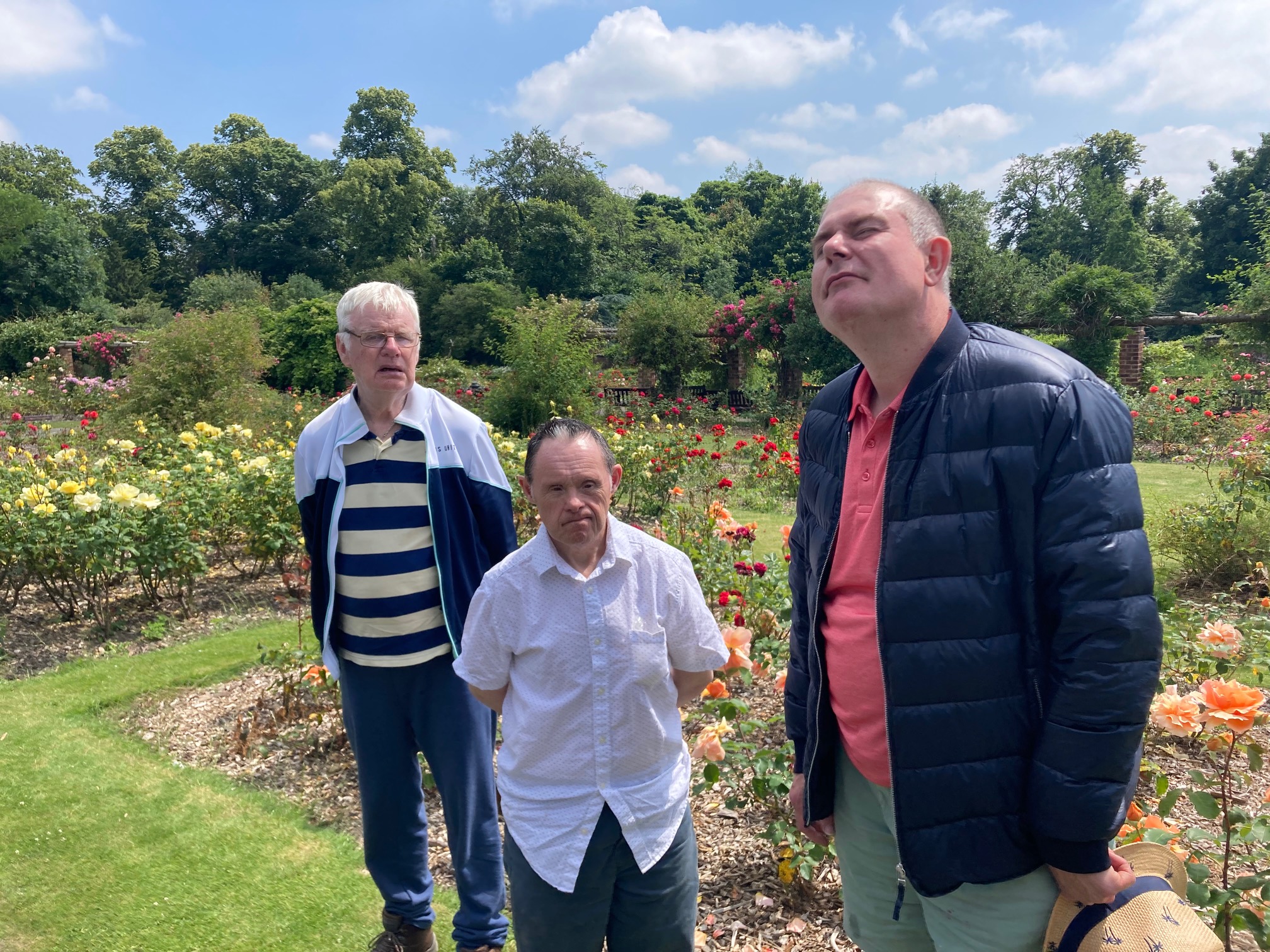 Three people standing in a rose garden in summer.