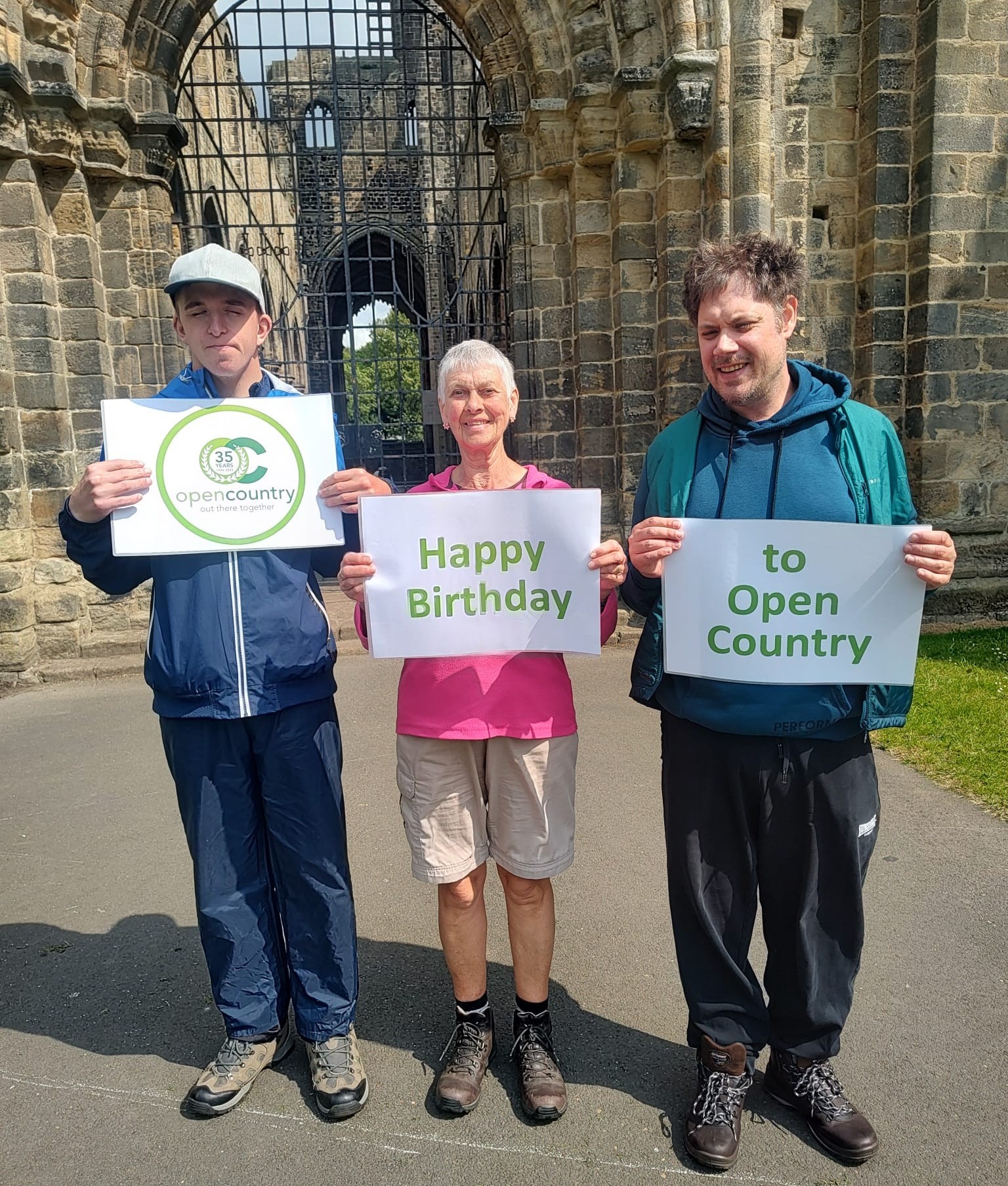 Three people outside holding up a happy birthday sign