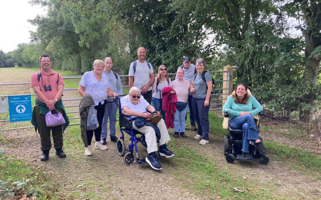 A group of people with differing abilities pose for a photograph in the countryside.